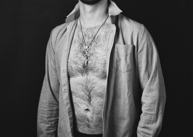Man with open shirt and necklace against dark background