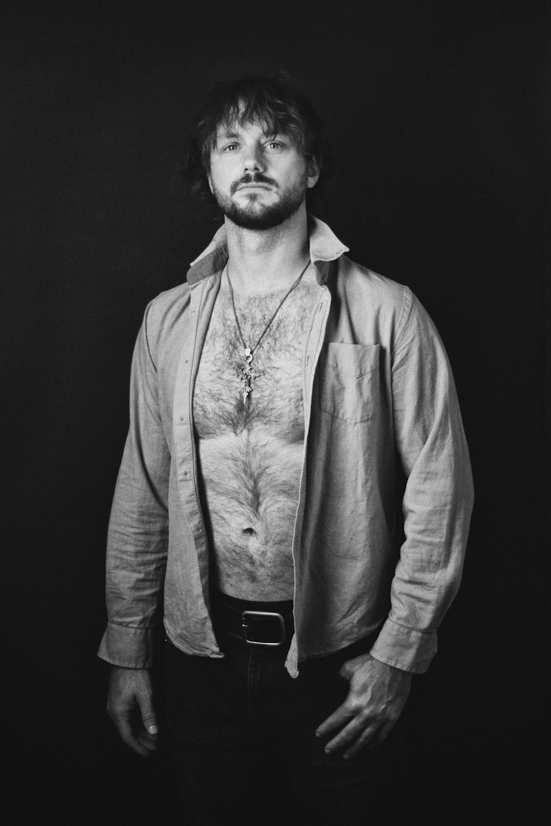 Man with open shirt and necklace against dark background
