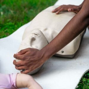 Hands practicing cpr on a training dummy outdoors