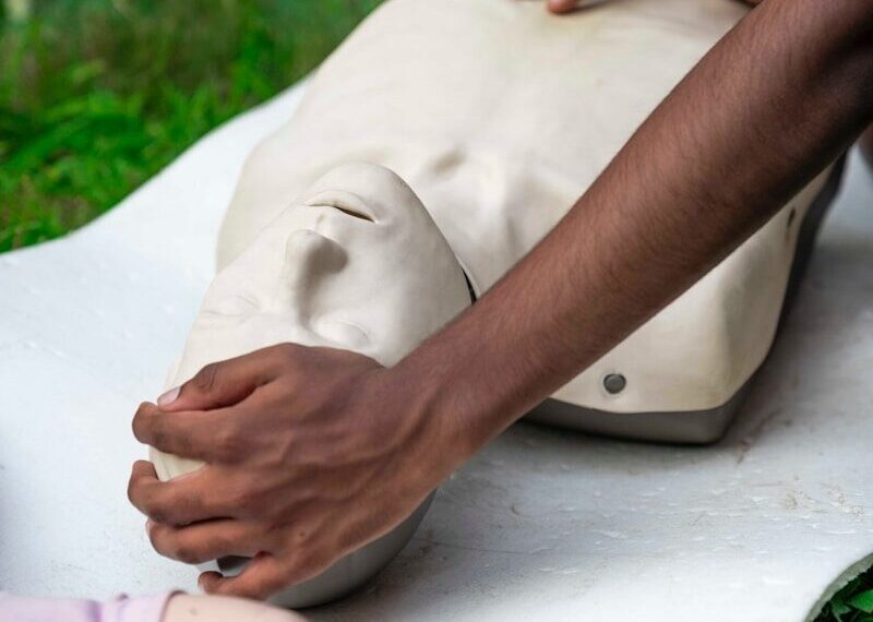 Hands practicing cpr on a training dummy outdoors